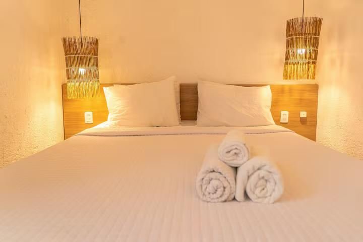 Suíte com cama de casal, luminárias de fibra natural e toalhas